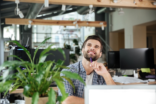 Homme pensant heureux dans le coworking de bureau tout en utilisant un ordinateur portable