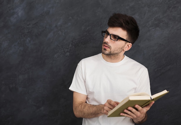 Homme pensif lisant un livre sur fond gris, copiez l'espace. Étudiant intelligent dans des verres se préparant aux examens