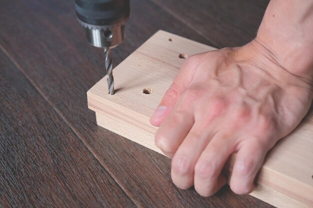 L'homme perce des trous sur une planche de bois pour la production de meubles artisanaux à la maison Meubles d'assemblage