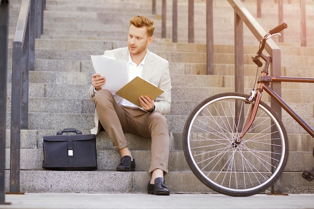 Homme perplexe en costume classique regardant des documents assis dans les escaliers