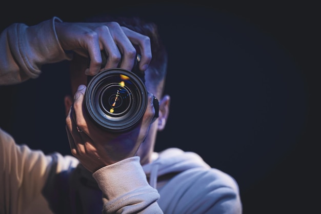 Un homme photographe avec un appareil photo prend une photo dans l'espace de copie sombre