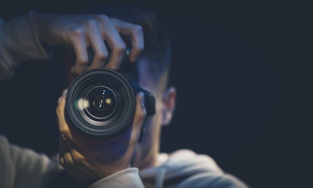 Photo un homme photographe avec un appareil photo prend une photo dans l'espace de copie sombre