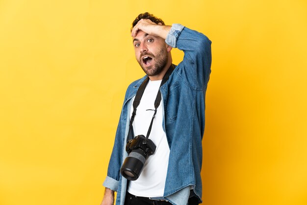 Homme photographe isolé sur fond jaune faisant un geste de surprise tout en regardant sur le côté
