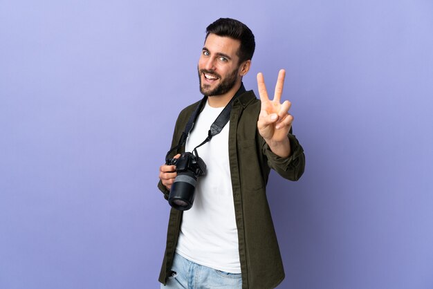 Homme photographe sur violet isolé souriant et montrant le signe de la victoire