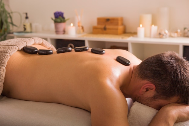 Homme avec des pierres sur la table de massage au spa avec traitement corporel. Personne allongée et relaxante lors d'un "massage aux pierres chaudes".