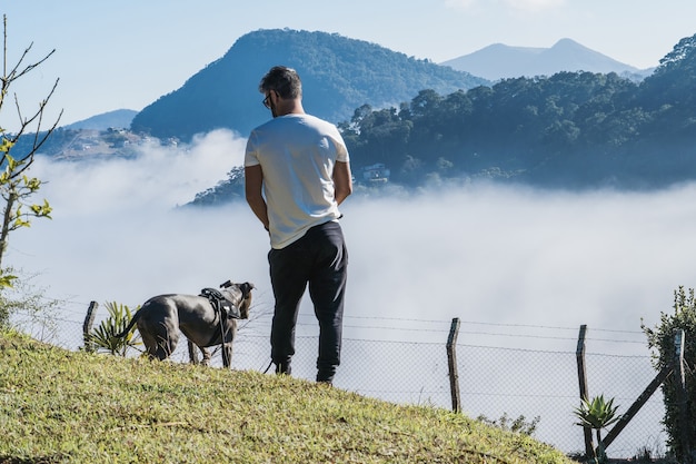 un homme et un pit-bull dog admirant la nature et le grand brouillard dans les montagnes de petropolis brésil