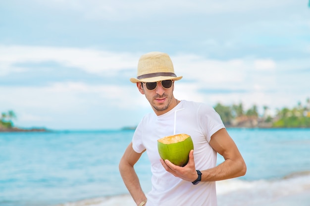 Un homme sur la plage boit de la noix de coco.