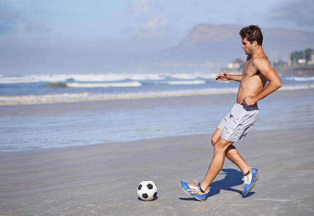 Homme à la plage et jouant au football pour les sports de jeu ou l'exercice dans l'entraînement ou la pratique de passe-temps en plein air Jeune homme ou joueur de football avec un ballon sur la côte de l'océan pour un match ou un entraînement cardio au bord de la mer