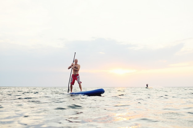 Homme sur une planche de SUP contre un beau coucher de soleil et la mer