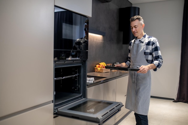 Homme avec une plaque à pâtisserie debout près d'un four ouvert