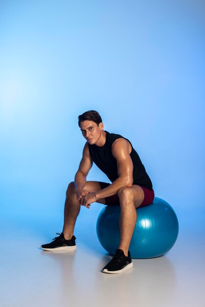 Photo homme plein coup assis sur un ballon de gym