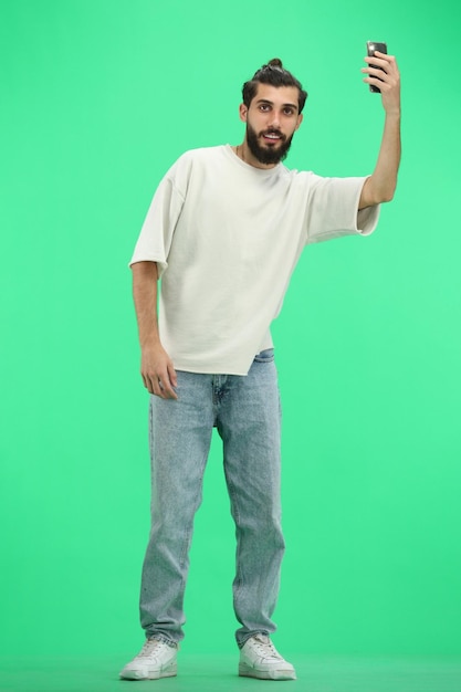 Un homme en pleine longueur sur un fond vert agitant son téléphone