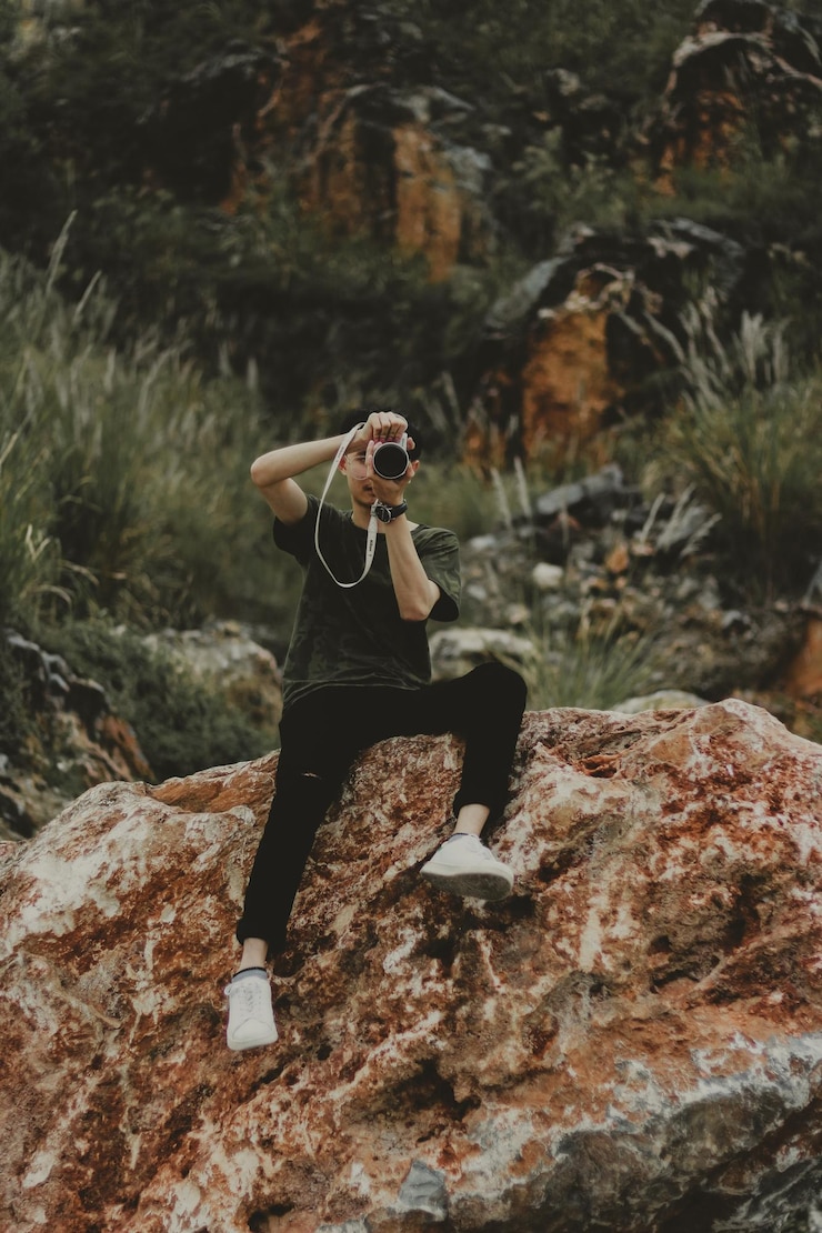 Photo l'homme en pleine longueur photographie alors qu'il est assis sur un rocher