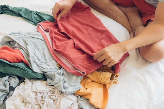 L’homme plie et range les vêtements sur le lit.