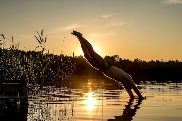 L'homme plonge dans l'eau du lac au coucher du soleil