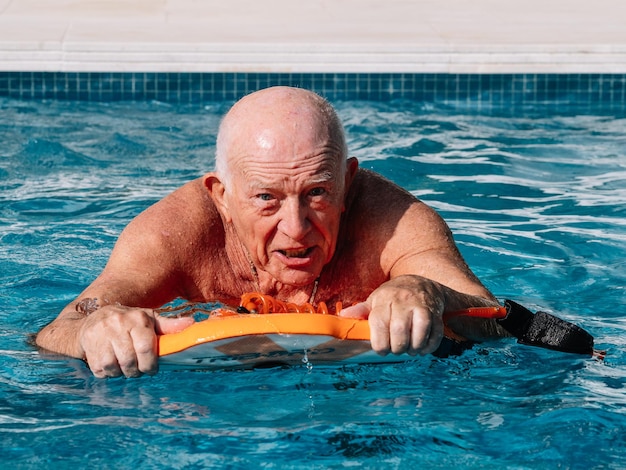 Homme de plus de 80 ans chauve exerce et nage avec un body board dans la piscine