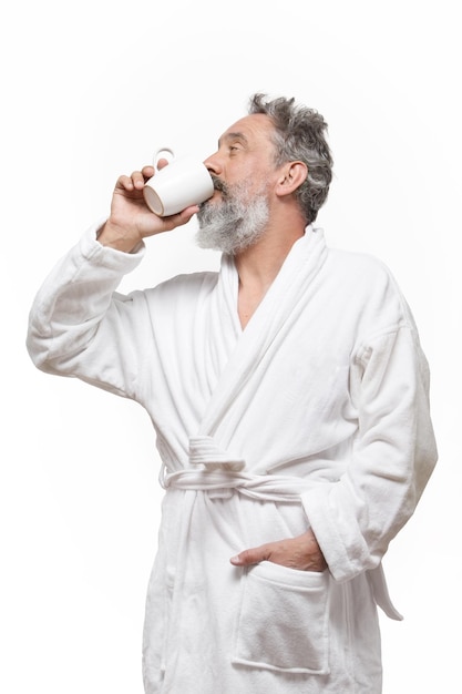 Homme plus âgé avec barbe en peignoir buvant une tasse de café avec un fond blanc