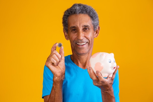 Homme plus âgé tenant une tirelire et une pièce brésilienne sur fond jaune. concept financier