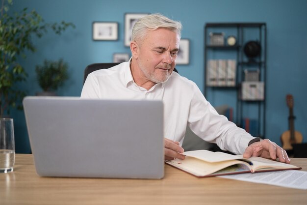 Homme plus âgé travaillant en ligne avec un ordinateur portable à la maison assis au bureau bureau à domicile naviguant sur Internet