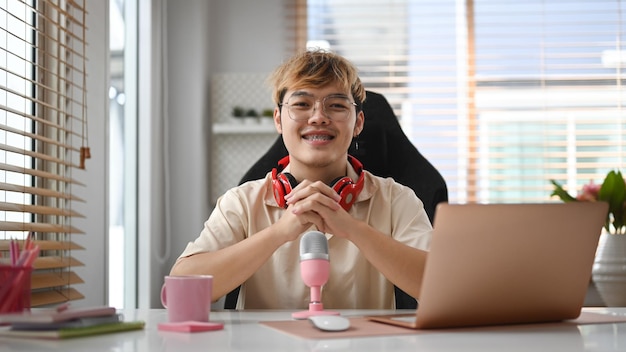 Homme podcasteur utilisant un ordinateur portable et un microphone enregistrant un podcast depuis un home studio