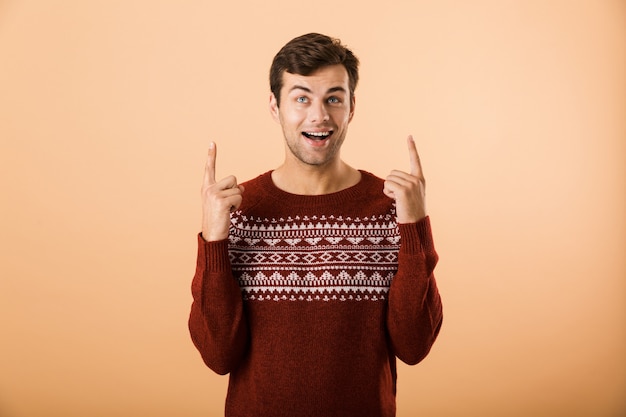 Homme avec poils portant un chandail tricoté doigt pointé vers le haut à copyspace, isolé sur mur beige