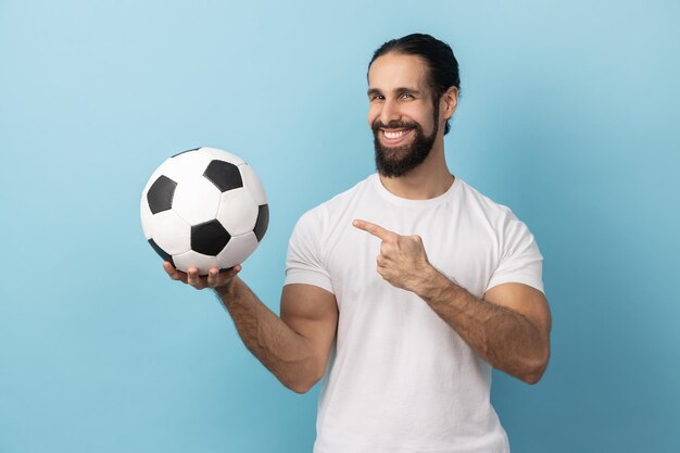 Homme pointant sur un ballon de football à la main et regardant la caméra avec un sourire à pleines dents