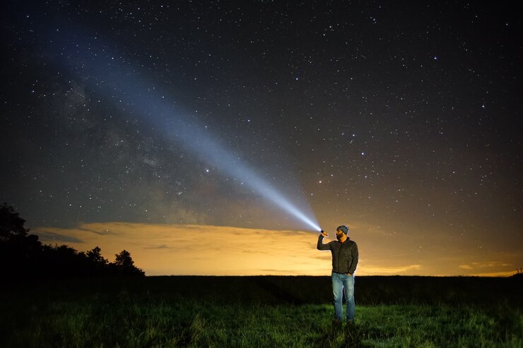 Photo homme pointant la lampe de poche vers le ciel la nuit.