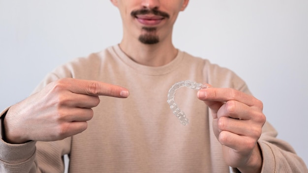 Homme pointant la main vers le dispositif de retenue d'aligneur dentaire sur la clinique dentaire de fond blanc