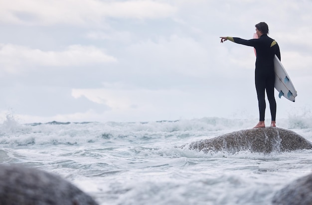 Homme pointant ou surfeur sur des rochers à la plage, à l'océan ou à la mer agitée et regardant les vagues de la marée ou le mouvement de l'eau à Hawaii