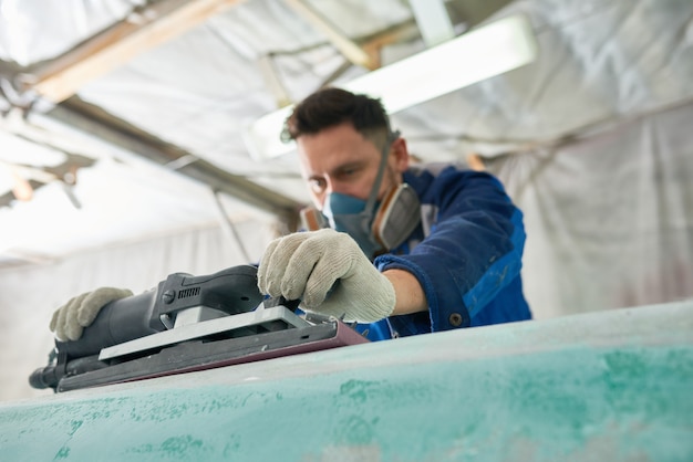 Homme polissant des bateaux en atelier