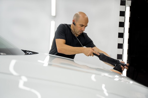 Homme polissant une voiture blanche, vêtu d'un t-shirt noir