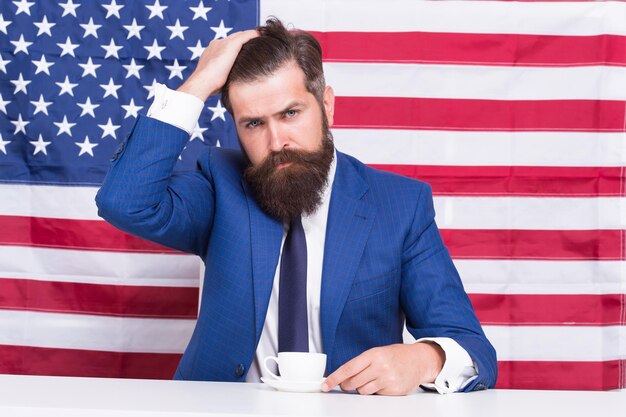 Homme politique américain en élection. sa campagne électorale. homme barbu boit une tasse de café. Réforme américaine de l'éducation le 4 juillet. Citoyen américain au drapeau américain. boire du café à la tribune.