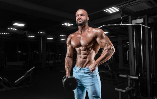 Homme pompé posant dans la salle de sport en jeans avec un haltère à la main