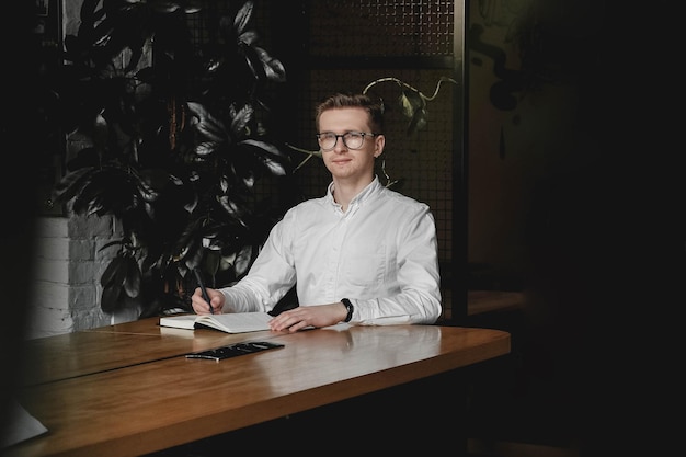 Homme portant assis à table tenant un stylo prend des notes sur son agenda sur un fond sombre au bureau