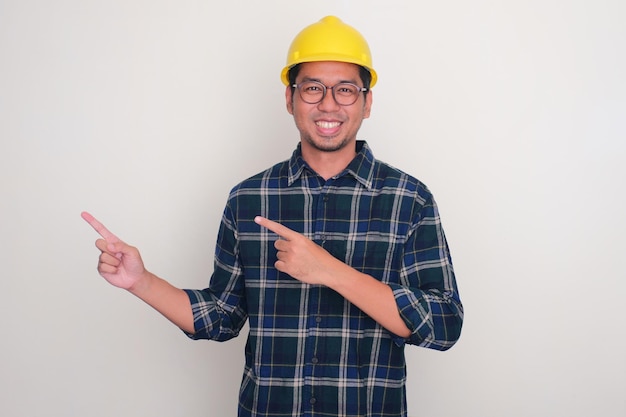 Un homme portant un casque de construction souriant et pointant les mains vers le côté droit