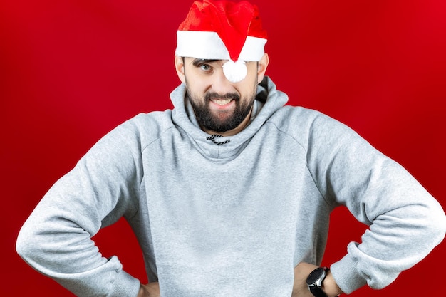 Un homme portant les chapeaux du Père Noël du Nouvel An et une chemise à carreaux rouge examine attentivement les jouets du Nouvel An - une boule de couleur or.