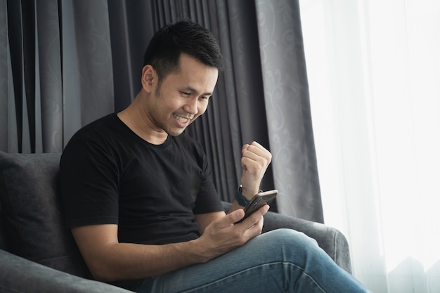 Homme portant une chemise noire en regardant le téléphone mobile et heureux