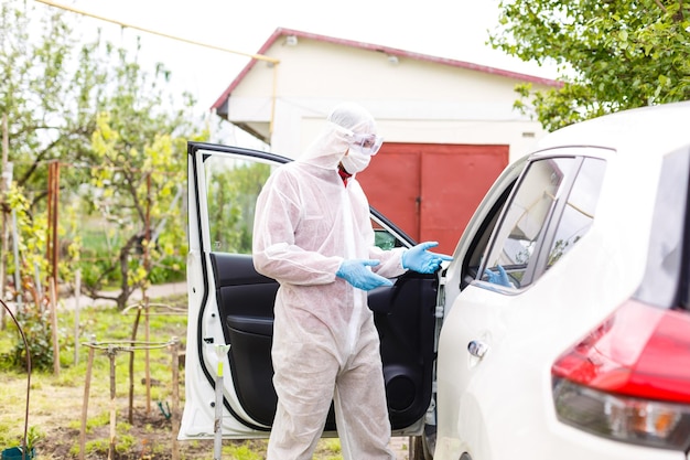 Homme portant une combinaison d'équipement de protection individuelle, des gants, un masque chirurgical et un écran facial, testant le coronavirus covid-19 sur un autre homme assis dans une voiture.