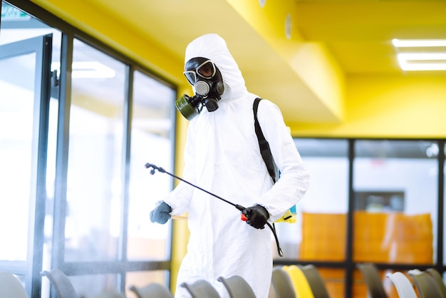 Homme portant une combinaison de protection désinfectant l'assemblage avec des produits chimiques en aérosol pour prévenir le coronavirus