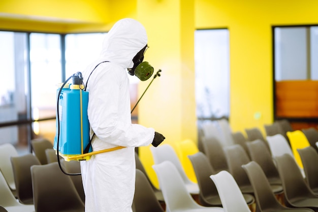 Homme portant une combinaison de protection désinfectant la salle de réunion avec des produits chimiques en aérosol empêchant le coronavirus