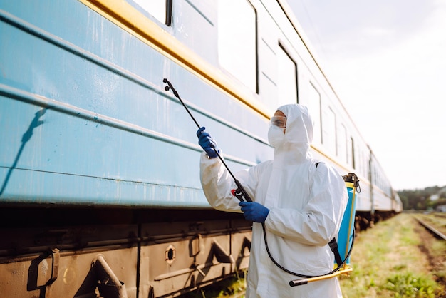 Homme portant une combinaison de protection désinfectant un train public.