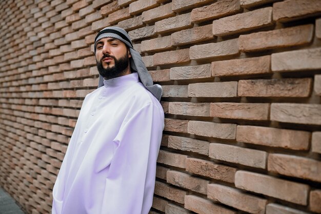 Un homme portant des couvre-chefs arabes traditionnels se tenant près du mur de briques