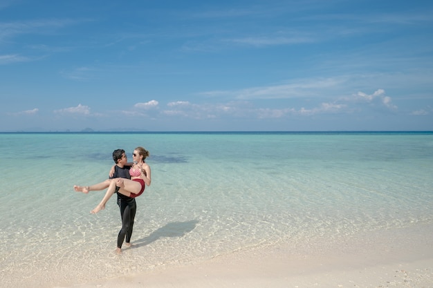 Homme portant femme bikini sur l'eau de mer par la plage de sable blanc. Paysage de mer et ciel bleu. vacances d'été.