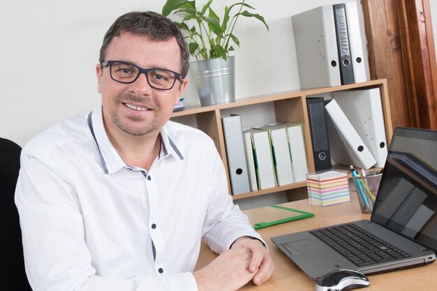 Homme, portant des lunettes et souriant, alors qu'il travaille sur ordinateur portable