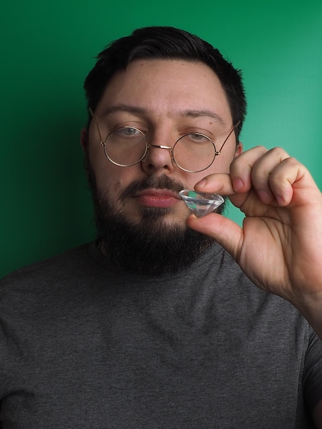 Un homme portant des lunettes tient un verre dans sa bouche.