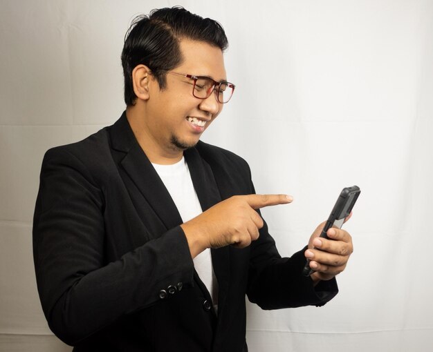 un homme portant des lunettes et une veste noire pointe un téléphone portable.