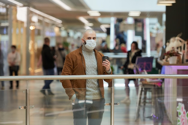 Un homme portant un masque facial pour éviter la propagation du coronavirus tient une tasse de café dans les magasins