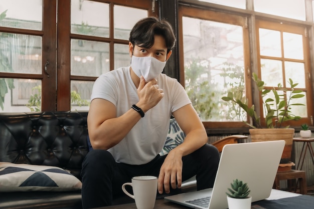 Un homme portant un masque facial travaille avec un ordinateur portable dans un café