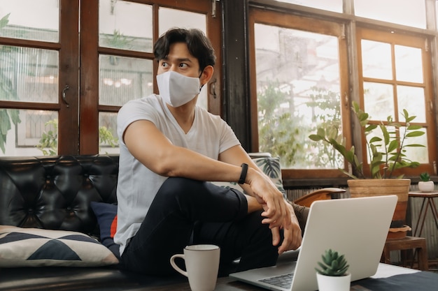 Un homme portant un masque facial travaille avec un ordinateur portable dans un café