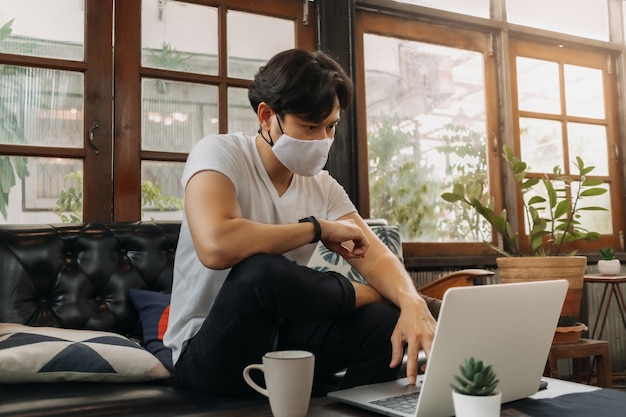 Un homme portant un masque facial travaille avec un ordinateur portable dans un café